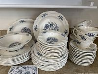 Wide view of multiple stacks of vintage Blue Dresden by Sheffield dish set showing plates, bowls, cups, and saucers grouped and stacked on a countertop.