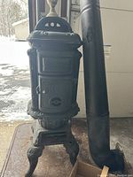 Full view of vintage cast iron wood stove with vent pipe attached around it, standing on base.