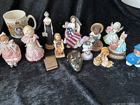 Wide view of all vintage figurines and commemorative mug on black cloth