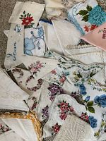 Photo showing a grouping of assorted vintage ladies handkerchiefs on carpeted floor with embroidered flowers, floral prints, and lace edges