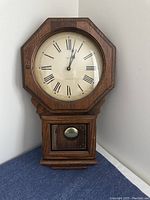 Full view of the Verichron octagonal wood wall clock showing the Roman numeral dial, pendulum window, and dark wood finish.