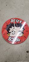 Front view of the round Betty Boop wall clock with red background and white clock hands showing approximately 4:00.