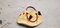 Vintage style chicken shaped purse lying on concrete floor, showing full body and red handles.