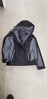 Full view of Free Country Radiance women's coat in size small laid flat showing black and gray exterior with hood and zippered pockets.