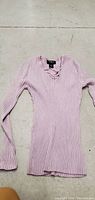 Full view of the medium pink long sleeve ribbed top laid flat on a rough surface, showing front detail and length.