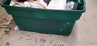 Green plastic storage bin filled with various folded towels in multiple colors.