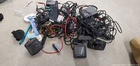 A pile of assorted electronic charging cables, plugs, adapters, and small electronic components scattered on a grey surface.