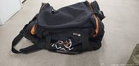 Men's black and orange gym duffle bag shown folded with visible zipper and strap details.