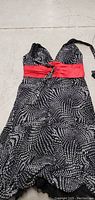 Front view of small women's dress showing black fabric with white dotted pattern and red waist tie