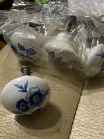 Close-up of round white ceramic knob with blue floral design and metal screw attached, part of 4-quantity group