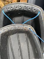 Close-up of the handle area of two torpedo branded snow sleds showing the brand embossed and blue pull rope tied through handle holes.