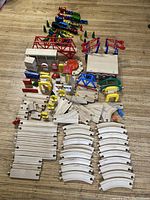 Overview of wooden train tracks, bridges, and buildings along with signs and accessories arranged on floor.