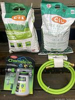 Photo showing two bags of CIL fertilizer (Purple Ply Lawn Food and Tree & Hedge Fertilizer) alongside a coiled bright green hose and packaged Chameleon hose end sprayer.