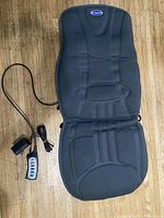 Full view of black Dr. Scholl's full-back massager cushion with attached wired controller on wood floor.