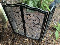 Front and side view of the black metal fireplace screen showing scrollwork design and mesh panels.