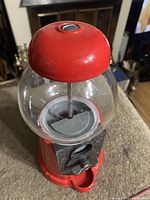 Front and side views of the glass bubble gum machine showing the glass globe, red metal base, coin slot, and dispensing area.