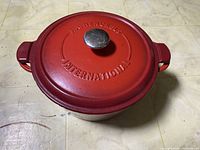 Top view of red enameled Henckel International Dutch oven with metal knob lid on a tiled surface.