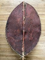 Full view of the oval-shaped leather shield with wooden spear attached down the center.