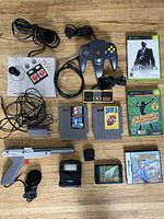 Overview photo showing all items in the lot including game controllers, games, and accessories arranged on wooden floor.