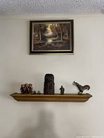 Wider wall view showing the oil painting hung above a shelf with various decorative figurines.