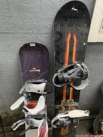Two Firefly snowboards standing upright, one smaller purple board with bindings and one larger black board with orange stripes and bindings.