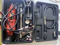 Black carrying case with red rotary tool and numerous accessories including flexible shaft, small vise, grinding stones, sanding drums, polishing pads, cutting discs, drill bits, and power cord.