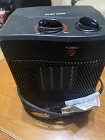 Close-up photo of the small black space heater showing front mesh, two control knobs, power light, and power cord.