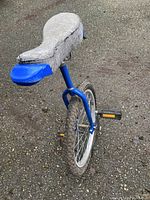 Full view of blue unicycle showing padded seat, wheel, and frame on asphalt surface.