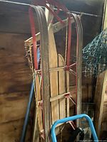 Full view of vintage wooden sled with red metal runners leaning against a wall in a rustic setting.