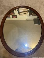 Front view of the oval wood framed mirror showing the reflective glass and polished wood frame.