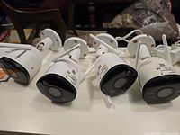 Four white cylindrical Defender Guard Pro CCTV security cameras lined up on a surface, showing the front sensor lens and mounting brackets.
