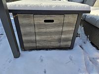 Front and side view of square fire pit table with snow cover, showing wood-look panels and metal legs