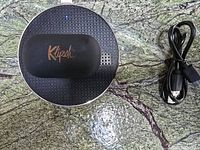 Large circular black and copper-colored wireless charging case with Klipsch logo and USB cable on granite surface.
