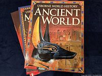 Four history books laid out showing covers with vivid illustrations of Ancient World, Medieval World, Roman World, and US-Born World themes