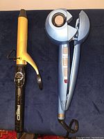 Photo shows two curling irons, a black and gold Dan Technology 1 1/4" curling iron and a blue BaByliss Pro automatic Nano-Titanium curling device.