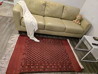 Photo showing the full rug placed on a floor in front of a beige couch, with visible fringe and pattern details.