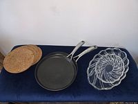 Full lot photo showing two cork trivets, two crepe pans, and two thick glass or crystal trays on a dark surface.