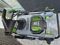 Overhead view of assembled snow blower showing chute, housing, folded metal handles and wheels.