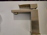 Photo of light gold faucet showing side profile with spout and handle on top, mounted on a flat surface with neutral background.