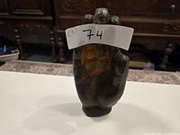 Front view of a metal Buddha hand sculpture with a label showing lot number 74, placed on a white surface.