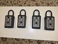 Four black combination lockboxes with numeric push-button locks arranged in a row on a white surface.