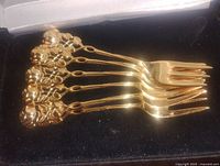 Set of six gold plated forks with ornate rose designs on the handles displayed in a box.