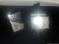 Two rectangular sterling silver cufflinks on a black surface, showing the front polished face with an engraved design.