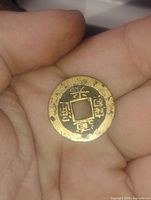 Bronze coin held in hand showing Chinese characters on obverse side with square hole in the center.