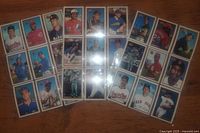 Three plastic binder sheets with a total of approximately 54 baseball cards featuring multiple players and teams laid on a wooden surface.