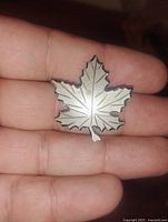 Front view of a sterling silver maple leaf brooch pin showing detailed leaf vein engravings held in hand.