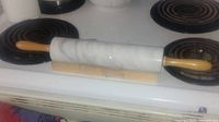 Photo showing the full view of the marble rolling pin with wooden handles placed on a stovetop.