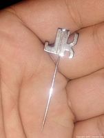Close-up photo showing the sterling silver J.K. initials stick pin held in hand, detailing the polished finish and shape of the pin.