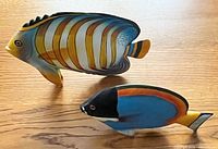 Photo showing two hand painted wooden tropical fish on a wooden surface, side view
