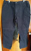 Full front view of black Carhartt carpenter pants hanging showing overall condition and style.